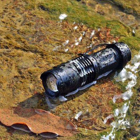 Ultra Bright Mini LED Flashlights 7W Zoomable Handheld Beams, Water Resistant, rugged, water-drenched flashlight on rocky surface.