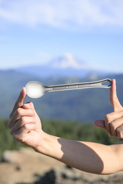 Person holding ultralight titanium long spoon for backpacking and camping, durable camp utensil with long handle and carabiner loop.