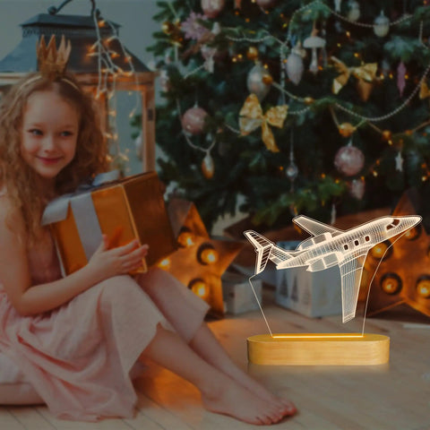 Lit 3D Airplane Illusion Night Light With Dimmable LED Wood Base beside a girl opening a gift near a Christmas tree