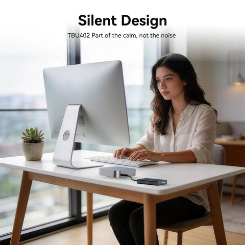 Woman working on a computer at a desk with a Blazing Fast 40Gbps NVMe M2 SSD Enclosure Handles Up To 8TB beside her.