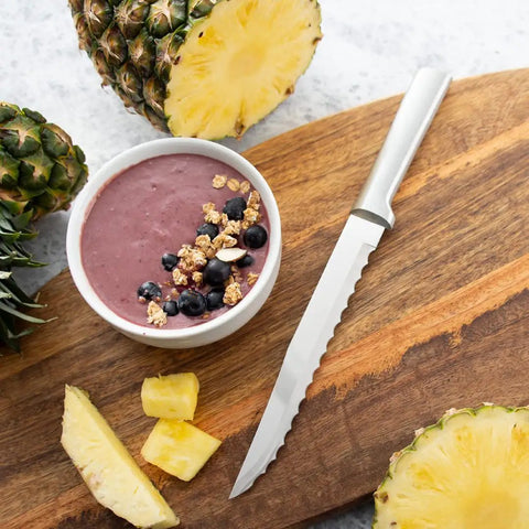 Smooth Serrated Slicer Knife With Knockout Double Sided Teeth That Crush Through Tough Produce Skins Like Hot Knife on wooden cutting board with fruits.