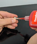 Threadlocker bottle dispensing red adhesive onto a metal bolt (front view)