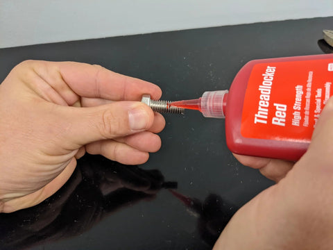 Threadlocker bottle dispensing red adhesive onto a metal bolt (front view)