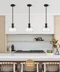 puncoll 2 PK 9 Inch Modern Black Clear Glass Pendant Light above a kitchen island with three pendant lights.
