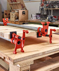 Bessey BPC-H34 3/4-in H-style pipe clamps in red, holding a wooden board on a workshop bench (angled view, five clamps).