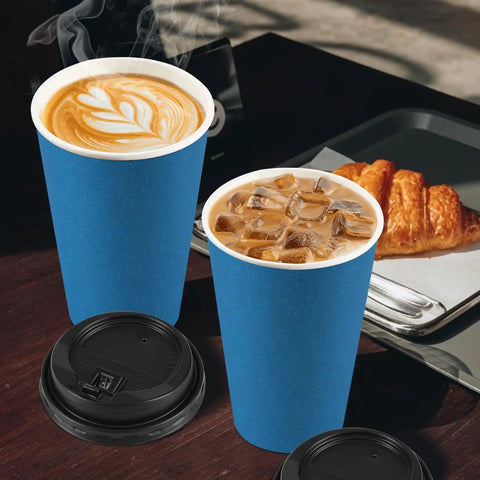 100 Pack 16 Oz Disposable To Go Coffee Cups With Lids, Sleeves And Stir Sticks For Grab And Go Hot Or Cold Drinks, Leakproof And Spill Resistant Paper Cups For Office Home Shop Events Navy with lids beside cups filled with hot coffee and iced coffee with a croissant on a tray in a cafe setting.
