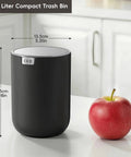 Compact Swing Top Mini Trash Can With Lid For Bathroom Vanity Countertop Desk Or Office 2.2L 7.3In Tall 5.3In Diameter Black Space Saver Tiny Trash Bin For Small Spaces next to an apple