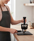 Slap On This Game Changing Espresso Pin Distributor And Coffee Wedge Tool That Knocks Out Clumps And Spreads Grounds Flawlessly For Barista Level Shots Without Breaking A Sweat At Home Or The Cafe In Sleek Black And 58mm used by a person on a kitchen counter.