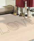 Basswood sheet 12 x 8 x 1/13 in being laser-engraved with the word LOVE.