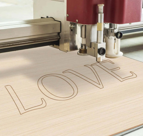 Basswood sheet 12 x 8 x 1/13 in being laser-engraved with the word LOVE.