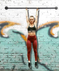 Person hanging from a horizontal bar against a graffiti-covered brick wall, exercising with stretched arms and legs.