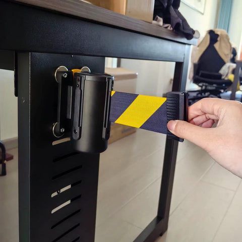 Slick Wall Mounted Retractable Warning Belt With Auto Magnetic Lock, Built Tough Five Meter Yellow And Black Barrier in use near a table.