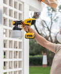 Man using 18V Cordless Paint And Stain Sprayer Delivering Slick HVLP Coatings on outdoor white lattice fence.