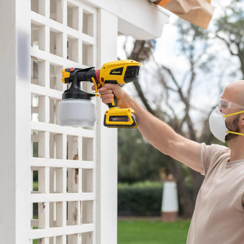 Man using 18V Cordless Paint And Stain Sprayer Delivering Slick HVLP Coatings on outdoor white lattice fence.