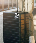 Compact Black And White Piano Grid Print Luggage Tags With Personalized Name Tags attached to a black suitcase in a travel setting.