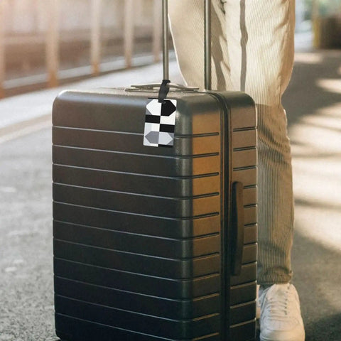 Compact Black And White Piano Grid Print Luggage Tags With Personalized Name Tags attached to a black suitcase in a travel setting.