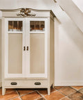 White vintage cabinet under stairs with glass pane doors and decorative charm on top