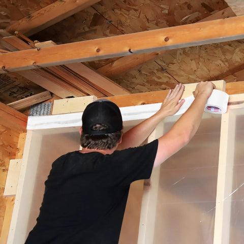 Person applying White Vapor Barrier Tape 9 Mil Thick, 3.78-Inch by 60-Yards Waterproof Moisture Barrier to construction wall.