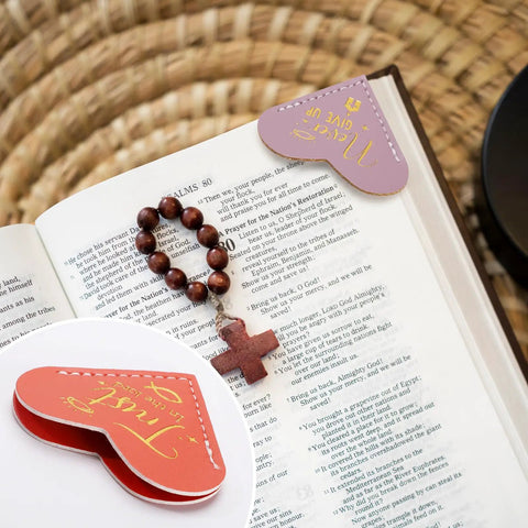 Fourteen Genuine Leather Heart Bookmarks With Uplifting Bible Verses marking pages in a book, showcasing soft texture and gold accents.
