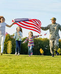 Family running with 3x5 Ft Heavy Duty Outdoor American Flag Deluxe Spun Polyester Waterproof UV Resistant Embroidered Stars in a park.