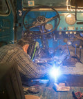 Welder using Flux Core MIG Wire For Mild Steel E71TGS 0.030 Inch, 2 Pound Spool inside a vehicle interior, sparks visible
