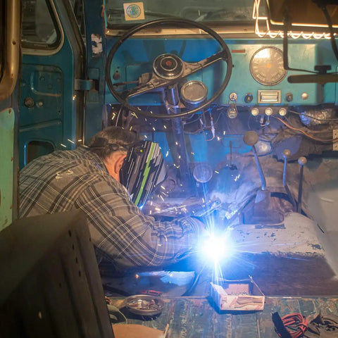 Welder using Flux Core MIG Wire For Mild Steel E71TGS 0.030 Inch, 2 Pound Spool inside a vehicle interior, sparks visible