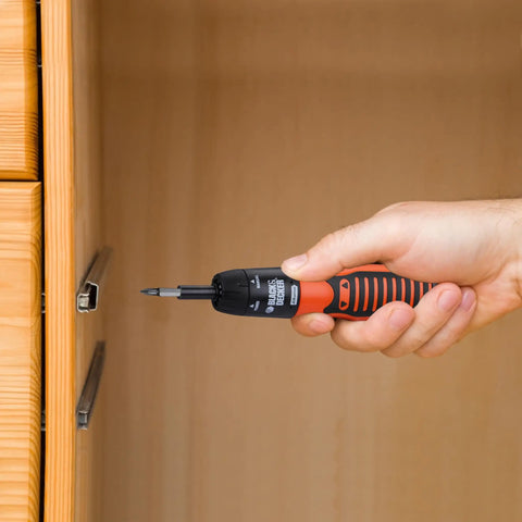 Hand holding Grab And Go 6V Cordless Screwdriver Kit With 14 Bit Set against wooden cabinet for quick home repairs.