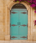 Turquoise double doors with iron strap hinges and handles set in a stone wall with purple flowers climbing on the side.