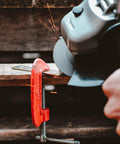 Angle grinder with a 4-1/2-inch flap disc grinding metal, sparks flying, secured in a red C-clamp vise.