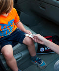 Parent handing adhesive strip to child next to 125 Piece Roadside Emergency Kit For Cars With Headlamp First Aid Tools And Visibility Gear.