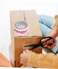 Fragile Warning Packing Tape Set With 5 Rolls being used to seal a cardboard box, with scissors cutting the tape, ensuring safe parcel handling.
