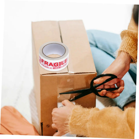 Fragile Warning Packing Tape Set With 5 Rolls being used to seal a cardboard box, with scissors cutting the tape, ensuring safe parcel handling.