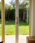 Natural Solid Wood Sliding Patio Door Handle With Ergonomic Curved Grip installed on glass door with chrome brackets.