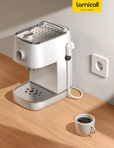 Compact white coffee machine with a cup of coffee on a wooden counter next to a wall plug.