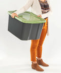 Heavy Duty 17.5 Gallon Plastic Storage Bin With Clear Lid And Full Length Through Wall Handles Gray Opaque Base held by a person.