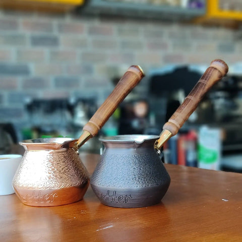 Two DCS Series Thickest Hammered Copper Turkish Greek Arabic Armenian Coffee Pot With Wooden Handle For Stovetop Brewing 20 Fl Oz Cezve Jezve Ibrik Briki Pro Grade on a table.