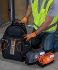 Person using a black heavy-duty backpack with gray and orange dual compartment tool pouch, ideal for meters and gear.