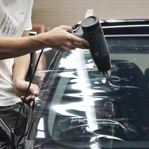Person using 1800W heat gun from All In One Car Vinyl Wrap Tool Kit With 1800W Heat Gun Felt Squeegee Plastic Scraper Utility Knife And Vinyl Wrap Gloves For Easy DIY Auto Film Installation on car windshield