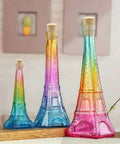 Three colorful Eiffel Tower-shaped bottles with cork stoppers on a table, decorated in rainbow hues with a textured design.