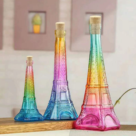 Three colorful Eiffel Tower-shaped bottles with cork stoppers on a table, decorated in rainbow hues with a textured design.