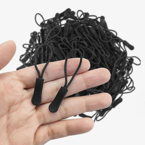 Hand holding two black zipper pulls from 20 Piece Zipper Pull Replacement Kit For Jackets Luggage And Backpacks Black Zipper Pull Tabs For Repair