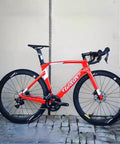 Red road bike with Classic Pro Carbon Wheelset With Deep 38, 50, 60, 88mm Depth For Rim Brake Road Bikes, parked on stone pavement.