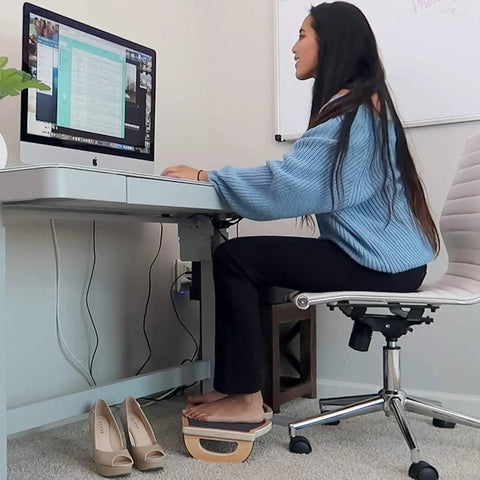 Woman using Ergonomic Wood Foot Rest With Rocker Board For Standing Desks, Supports Up To 350 Lbs, Non Slip, 18 Inch Wide under desk