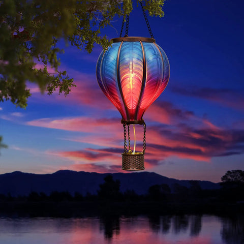 Blue Purple Hot Air Balloon Solar Lantern for Garden Decor lit at sunset by a lake with hanging chains and flickering flame effect.