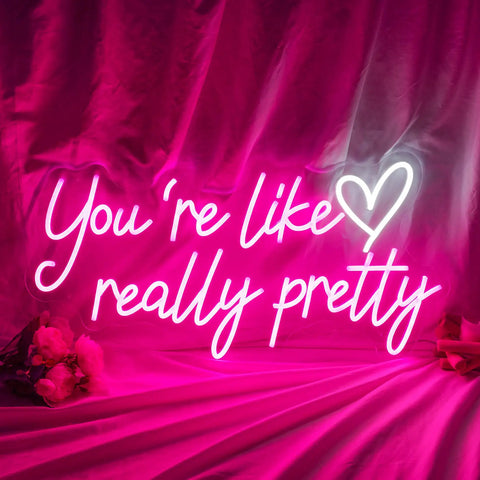 Lit Pink Neon Sign Youre Like Really Pretty Wall Decor LED Light Up Sign glowing against pink backdrop with flowers