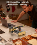 Artilume T1 foldable laser engraver on a workbench; gold-gray metal frame with rails beside wooden ornaments.
