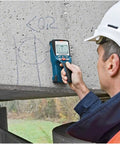 A contractor using a wall scanner on concrete to locate hidden objects, featured in Nail Your Next Home Project Straight Up With This Hella Reliable Wall Scanner And Metal Detector Featuring Millimeter Exact Center Targeting For Busy Contractors.