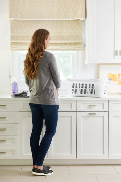 Woman with long hair stands by hip hugger laundry basket with easy one hand carry grip one and a half bushel white hamper on counter