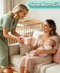 Two women, one holding a baby, exchanging a gift labeled 'New Mom Gifts' in a cozy, well-lit living room.