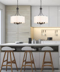 Kitchen with Totally Chic Modern Farmhouse Drum Chandelier with Linen Fabric Shades over island and stools, clean candle style look.